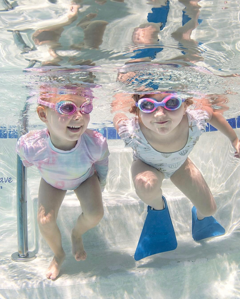 Two little girls smiling underwater wearing pink goggle and blue swim fins