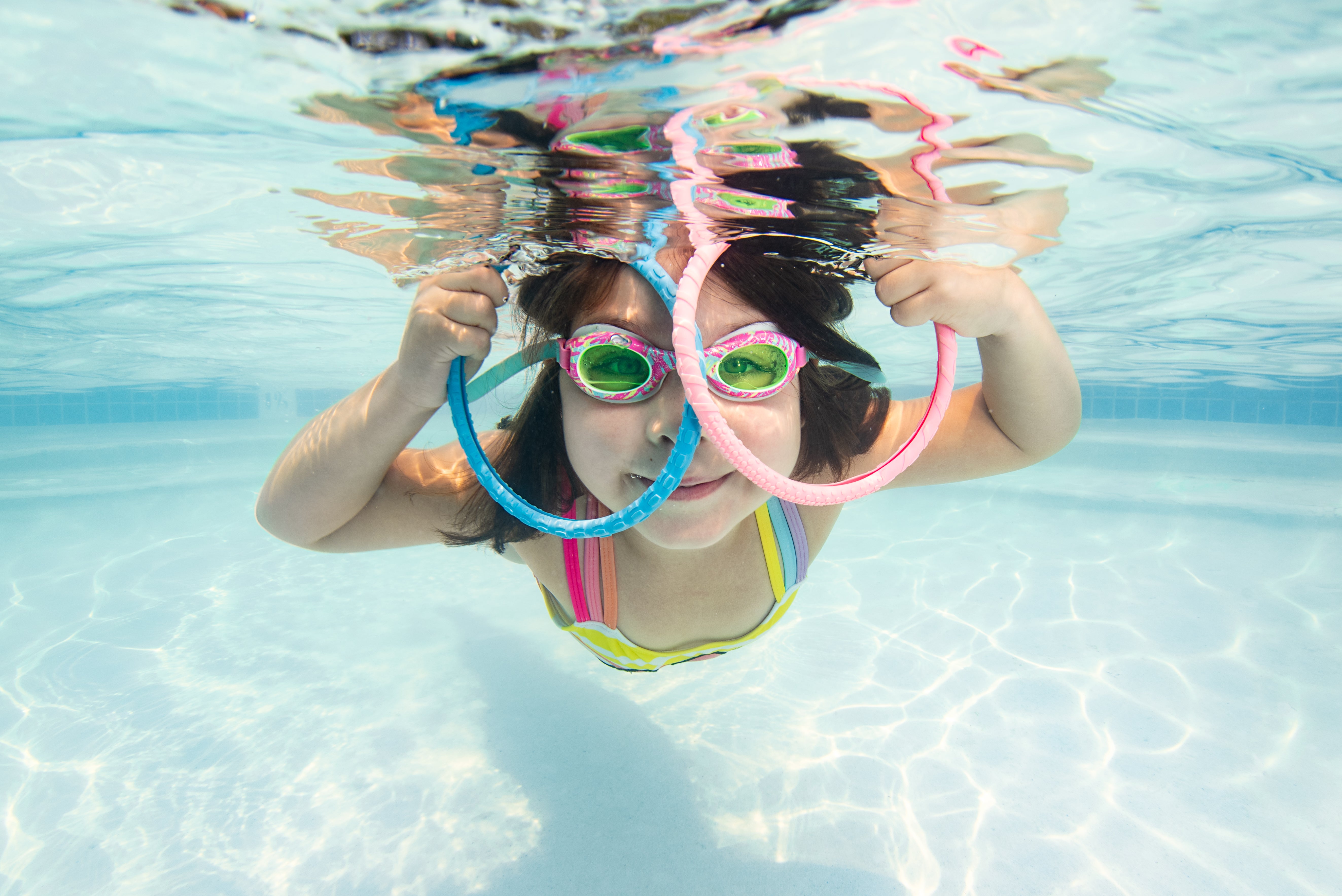 A girl swims underwater with two rings at Makai Swim School.